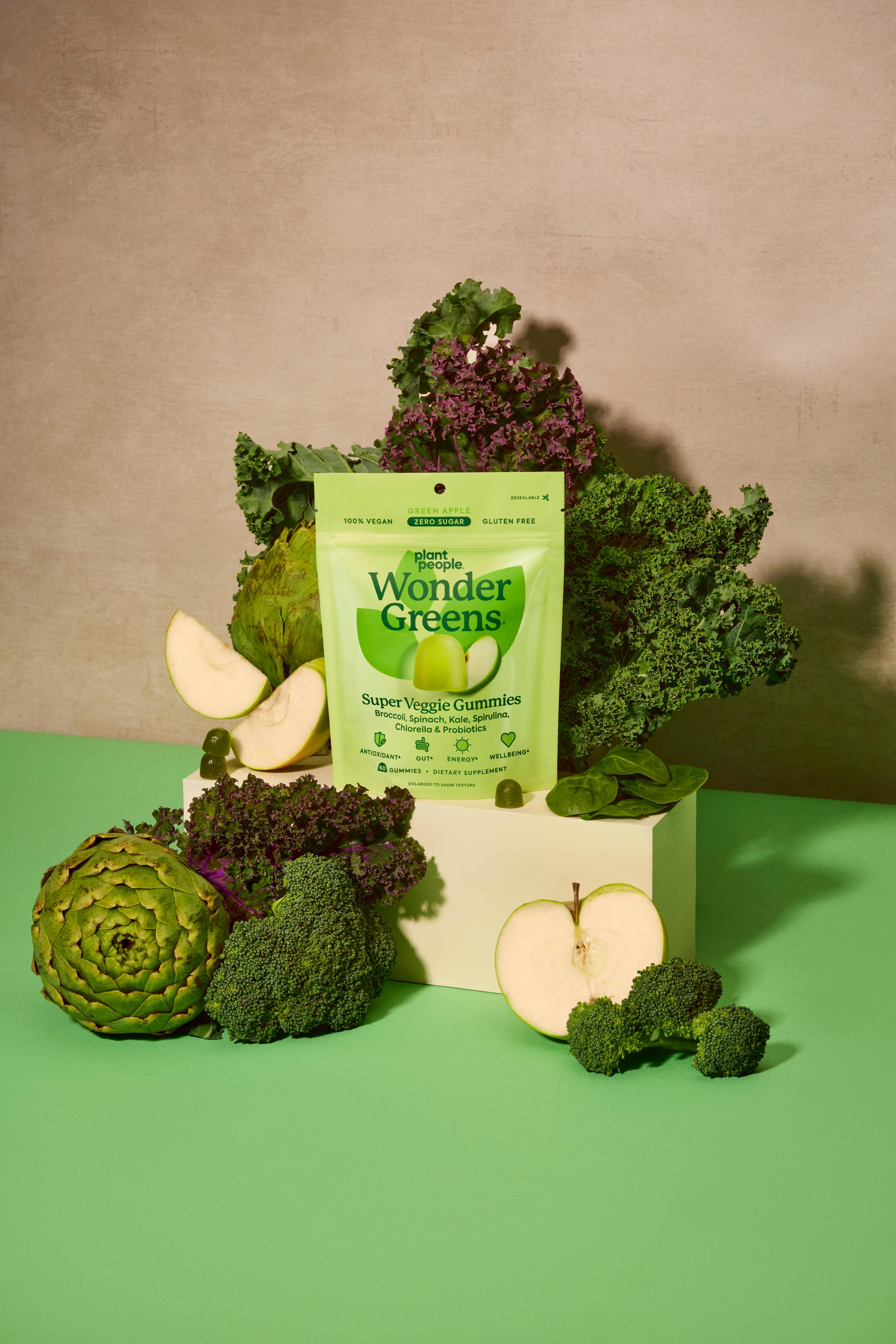 Bag of Wonder Greens super greens supplement surrounded by green vegetables on a green surface with a beige background
